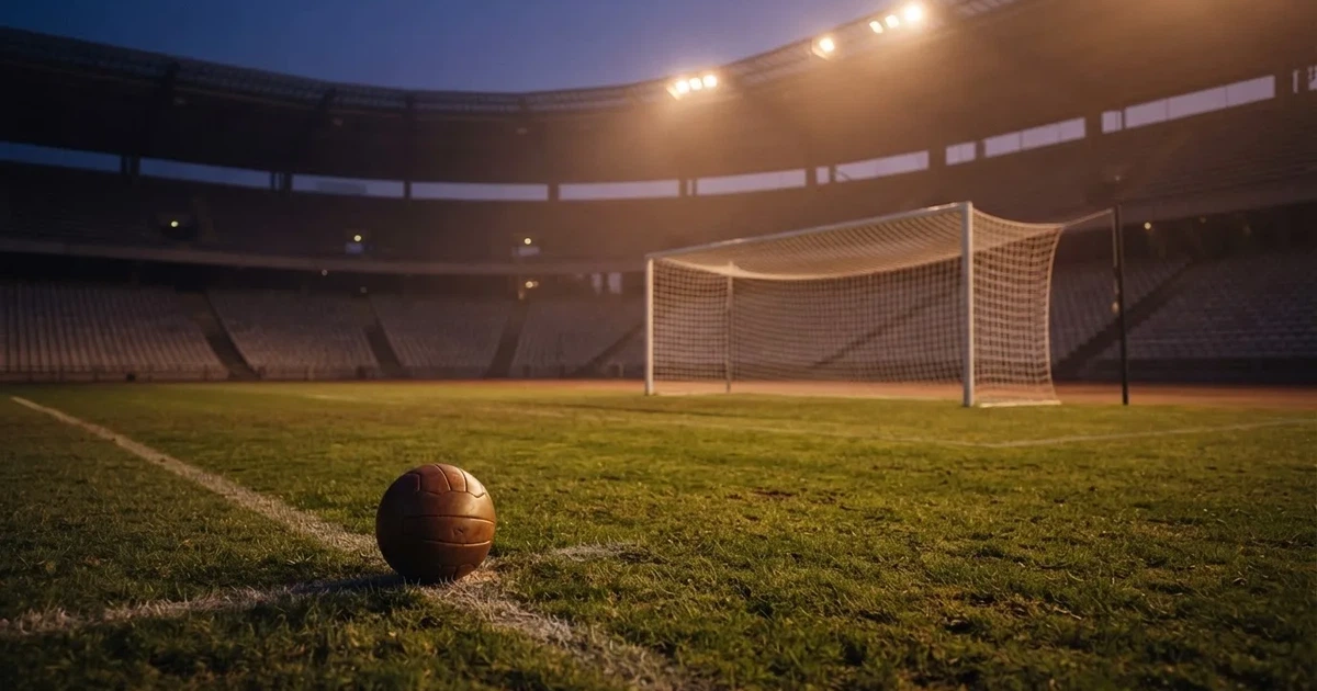 Ein Fußball liegt im Strafraum direkt vor dem Tor mit Netz, im Hintergrund leere Ränge bei Dämmerung.